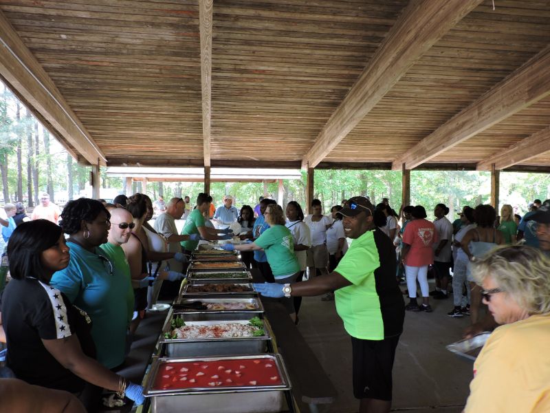 Line of people serving food out of metal containers to a large group