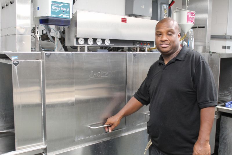 Man in a Black Shirt Standing in Front of Industrial Dish Washer in Kitchen