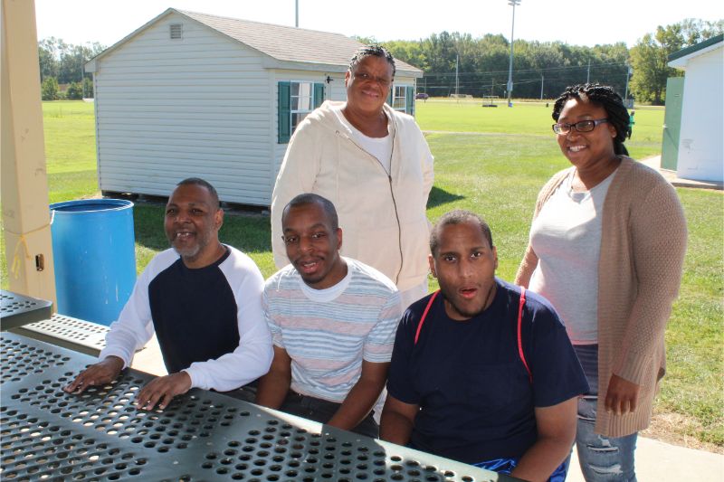 Three men Sitting on a Park Bench and two Woman Standing Behind them Posing for Photo