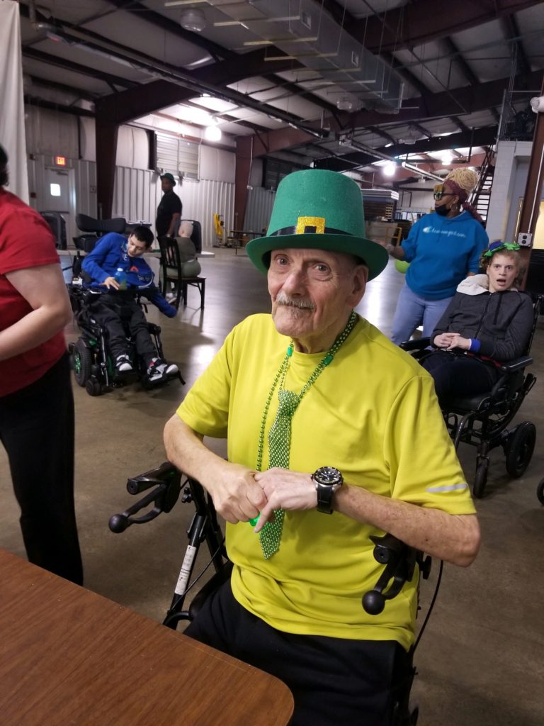 Older Man Sitting Down on a Chair Wearing Green Irish Hat and Green Beaded Tie